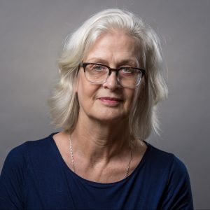 Photo of Lianne. A smiling woman with silver hair, wearing glasses and a blue shirt.